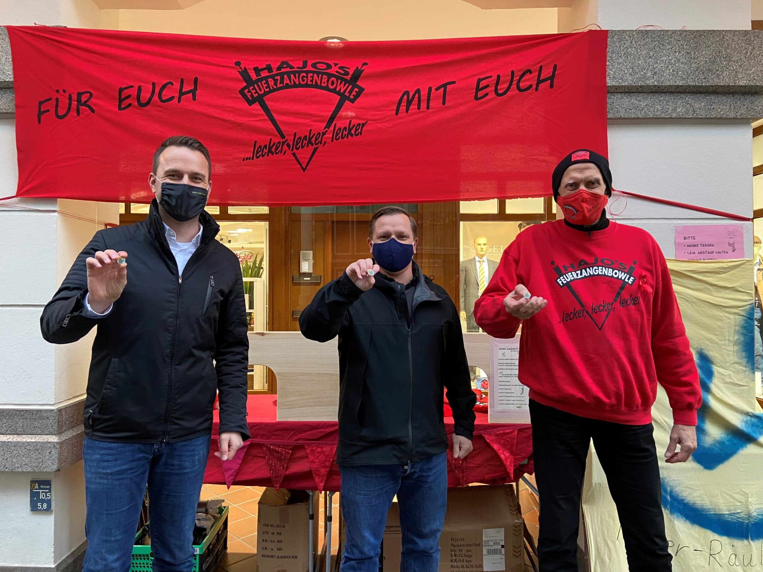 Dennis Berger und Andre Volke stehen zusammen mit Hajo - dem Wolfenbütteler Weihnachtsmarkt Standbetreiber Hajo vor seinem Stand und halten den Solidaritätspin hoch